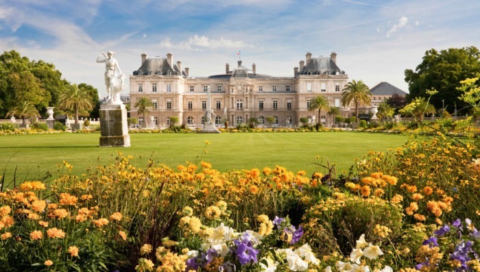 Jardin du Luxembourg with the Palace and statue. Few flowers are in front and blue sky behind.